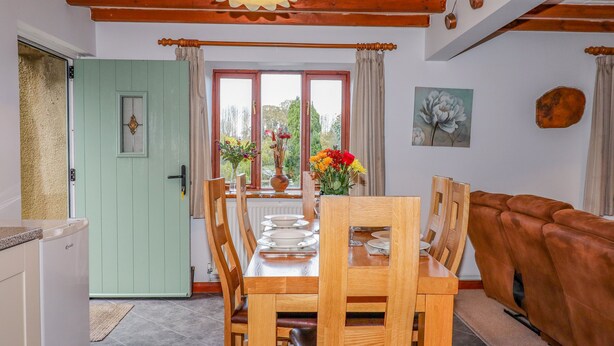 Un coin repas avec une table et des chaises en bois, une porte verte et une vue sur l’extérieur grâce à de grandes fenêtres.
