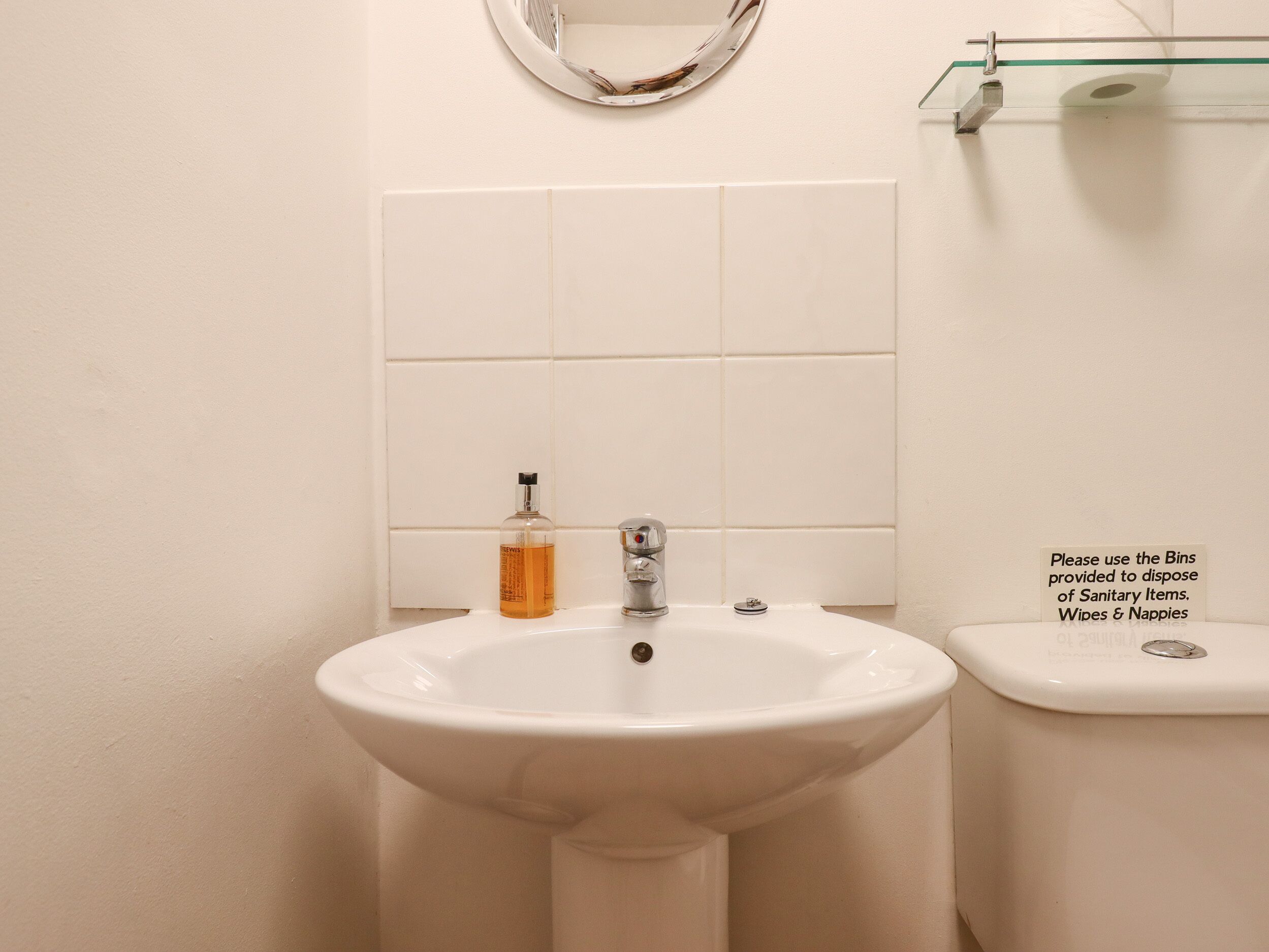 Ein Waschtisch mit Seifenspender, ein Spiegel und ein Schild mit der Bitte, Müllbehälter für Hygieneartikel zu nutzen.