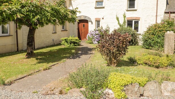 A stone building with a central door, surrounded by a gravel path and various shrubs. - 2 Yr Hen Felin (Haverfordwest)