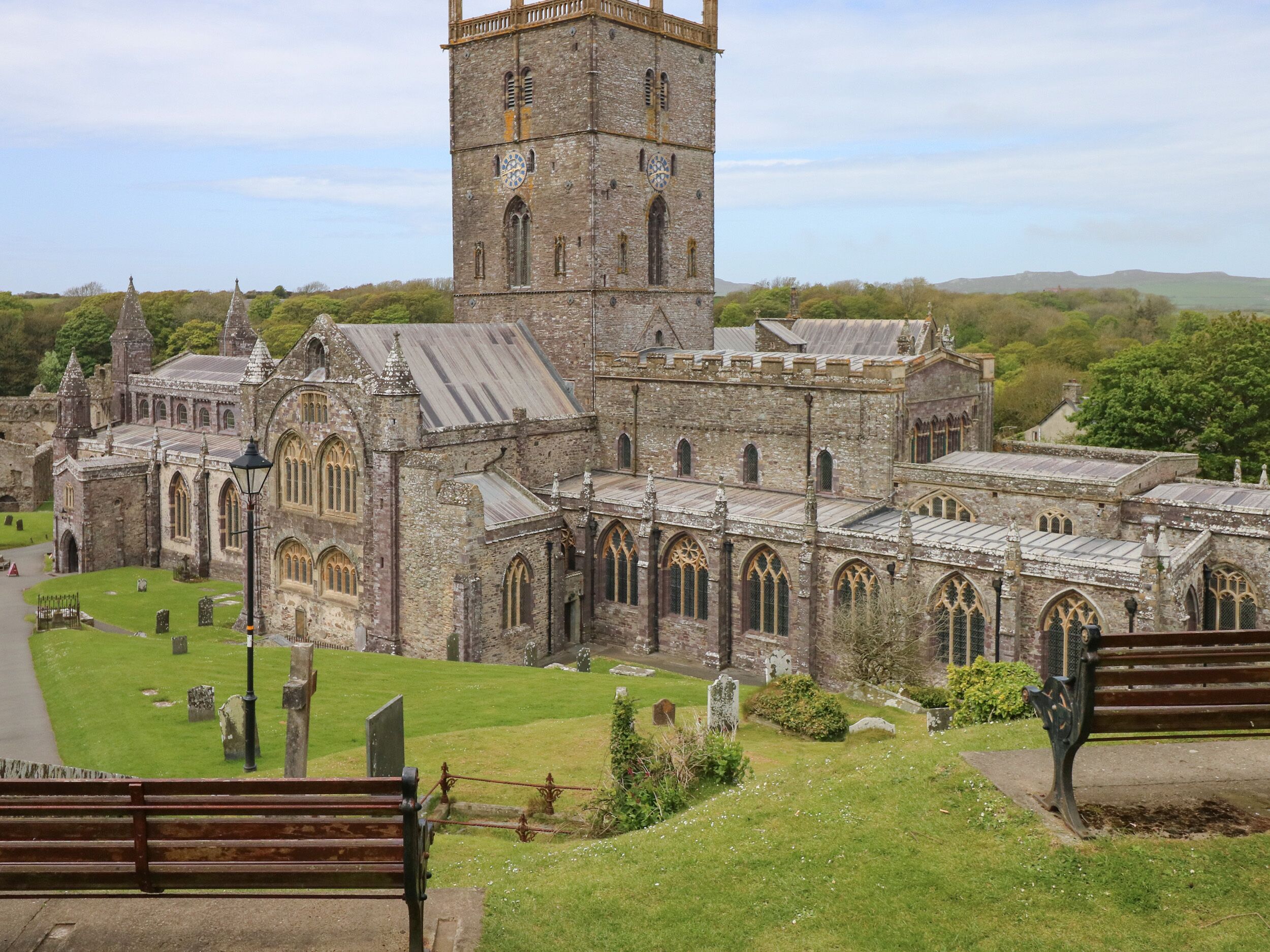 A historic stone building with a prominent tower, multiple arched windows, and a well-maintained lawn with benches.