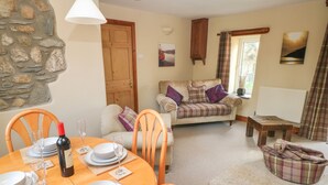 A cozy living room with a dining area, stone wall, wooden door, and a view of the outdoors. - 2 Yr Hen Felin (Haverfordwest)