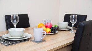 A dining table with white plates, bowls, and cups, accompanied by a fruit platter and two wine glasses.