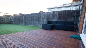 A wooden deck with a built-in seating area and a grassy yard enclosed by a wooden fence.