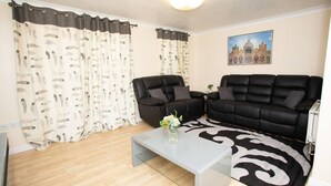A living room with two black sofas, a white coffee table, and patterned curtains.