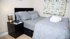 A neatly made bed with grey bedding, a black nightstand with a lamp, and a wall-mounted artwork.