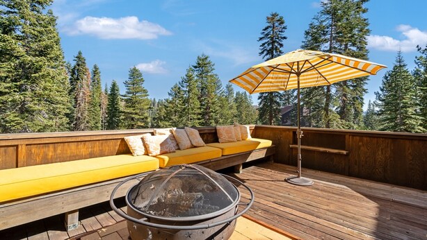 A deck with a yellow sofa, a fire pit, and an umbrella. - Walk to the Lake Amazing 5 Bedrm - VH#343 by Bear Valley Vacation Rentals (Arnold)