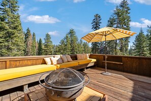 A deck with a yellow sofa, a fire pit, and an umbrella. - Walk to the Lake Amazing 5 Bedrm - VH#343 by Bear Valley Vacation Rentals (Arnold)