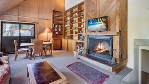 A cozy living room with a fireplace, wooden shelving, and a television. - Walk to the Lake Amazing 5 Bedrm - VH#343 by Bear Valley Vacation Rentals (Arnold)