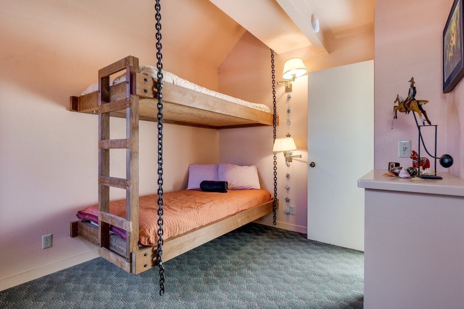 A bunk bed with a wooden ladder, a bedside lamp, and a small desk with decorative items.