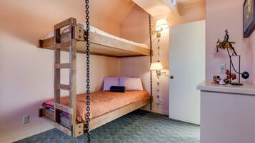 A bunk bed with a wooden ladder, a bedside lamp, and a small desk with decorative items.