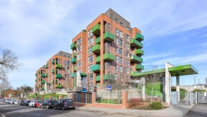 A multi-story residential building with balconies, a gated entrance, and a parking area with cars. - 2-bed Apartment Only 15 Mins From Central London (Wembley)