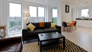 A modern living room with a black leather sofa, a coffee table, and a dining area with orange chairs. - 2-bed Apartment Only 15 Mins From Central London (Wembley)