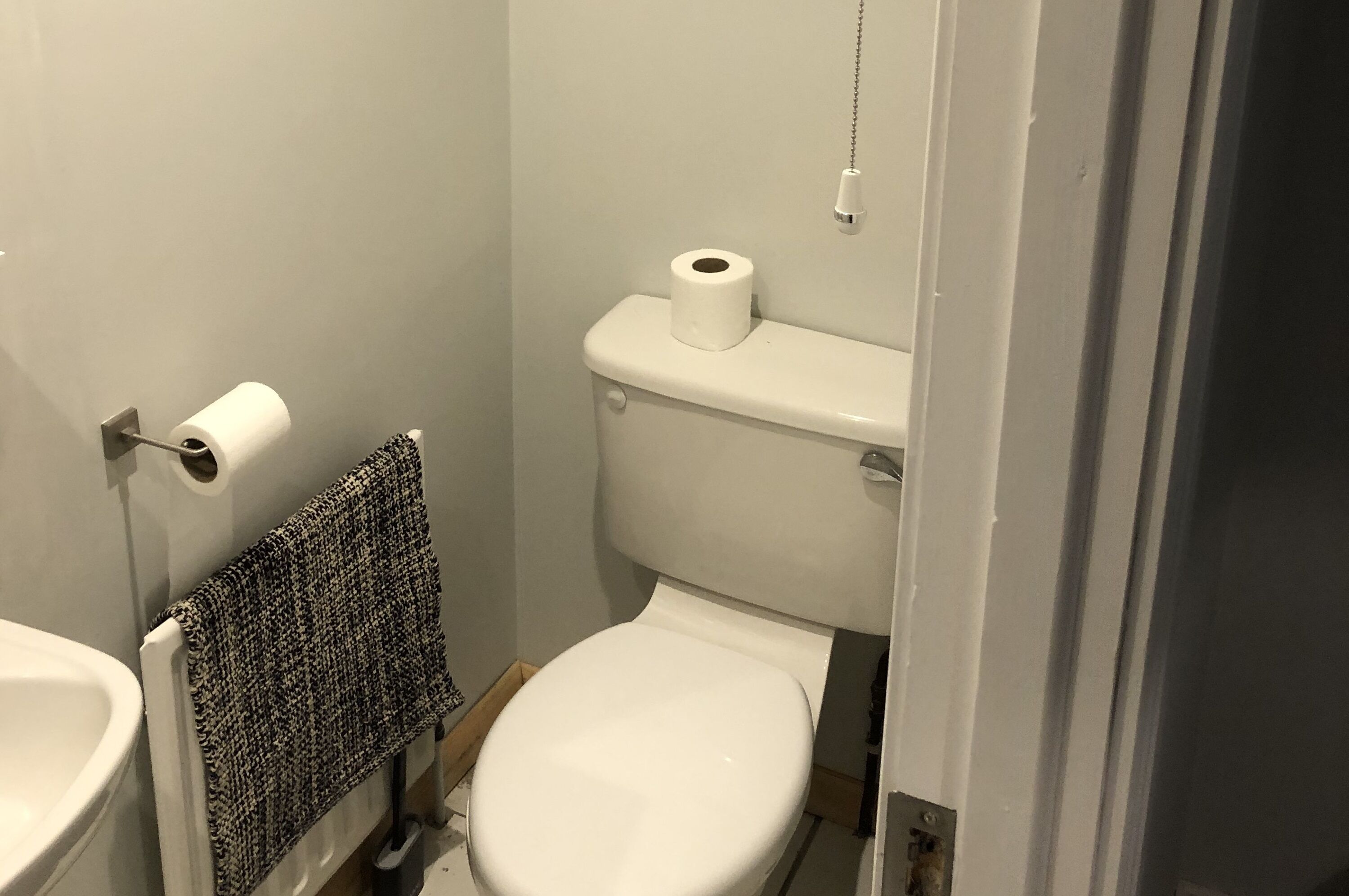 Un baño pequeño y funcional con inodoro, una toalla colgada en un perchero y un rollo de papel higiénico en la pared.