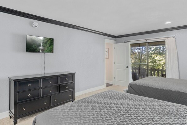 A bedroom with a TV, a dresser, two beds, a door leading to a balcony, and a ceiling light.