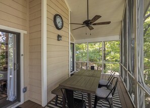 A covered porch with a wooden table and chairs, a ceiling fan, and a clock on the wall.