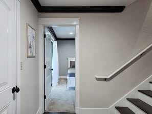 A hallway with a carpeted floor, a white door, and a staircase with dark steps.