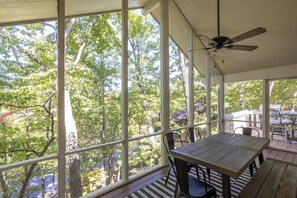 A covered patio with a table and chairs, large windows, and a ceiling fan.