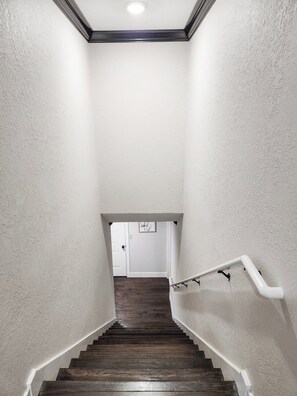 Un escalier aux murs blancs et au plancher en bois menant à une porte.