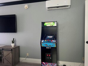 A room with a mounted air conditioner, a flat-screen TV, and a video game machine labeled 'Calzone.'