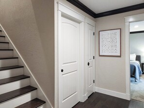 A hallway with a staircase, a white door, and a framed artwork on the wall.