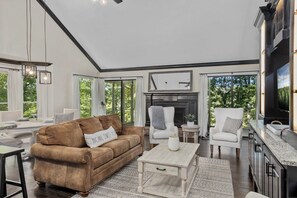 A spacious living room with a brown sofa, white armchairs, a coffee table, and a fireplace.