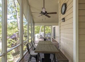 Une véranda abritée avec une table et des chaises en bois, un ventilateur de plafond et une horloge au mur.