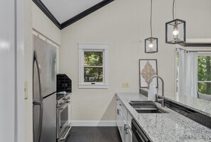 A kitchen with a refrigerator, stove, and sink. There is a window with a view of trees.