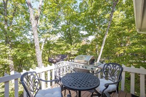 A covered outdoor area with a grill, metal chairs, and a white railing.