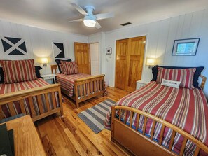 A cozy room with three wooden beds, each with striped bedding. There is a ceiling fan, a wooden door, and a framed picture on the wall. - The Circle R - Cozy 3 bedroom oceanside beach cottage w/Private Pool & Dogs Allowed (Southern Shores)