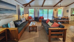 Una sala de estar acogedora con dos sofás, una mesa de centro y una chimenea. Hay un comedor con una mesa y sillas. La habitación tiene ventanas grandes y vistas al exterior.