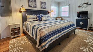 Un dormitorio con cama, mesitas de noche, televisión y decoración en la pared.