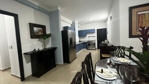 A modern kitchen with a refrigerator, oven, and sink. There is a dining table set with plates, glasses, and cutlery.