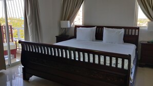A bedroom with a wooden bed, a nightstand, a lamp, and a view of the outside.