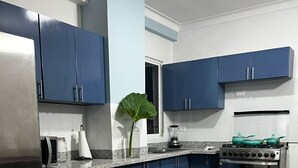 A kitchen with blue cabinets, a stainless steel refrigerator, a stove, and a microwave.