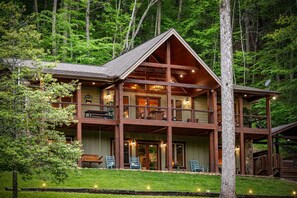 Eine zweistöckige Holzhütte mit Balkon, umgeben von einem Wald.