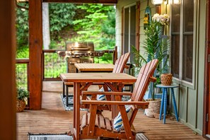 Eine Holzterrasse mit Tisch, Stühlen, einem Grill und Kübelpflanzen.