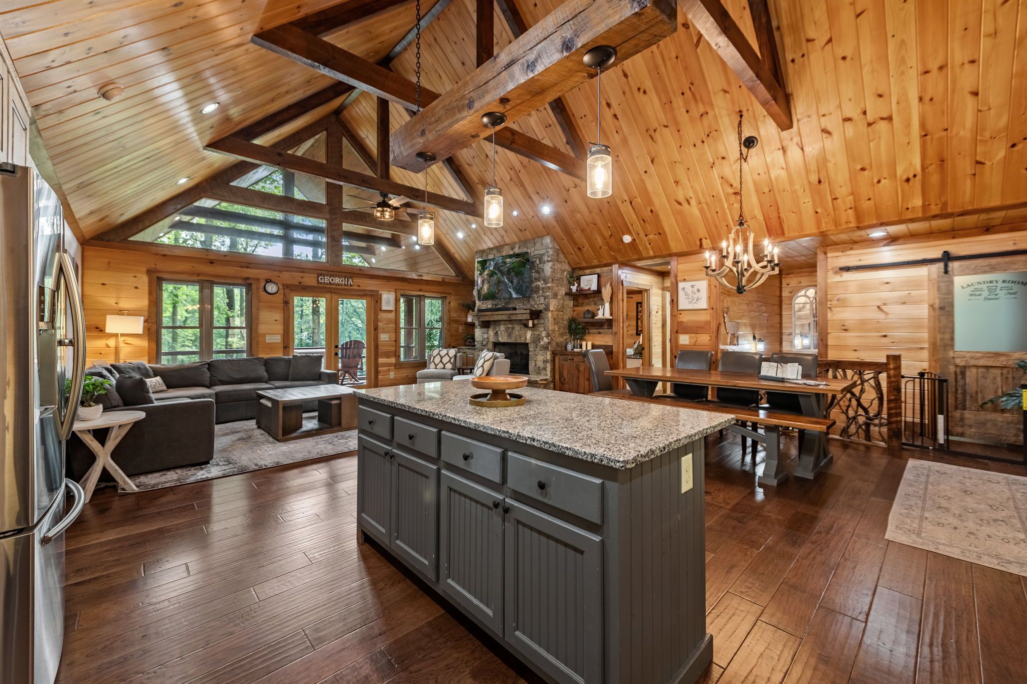A spacious kitchen with a large island, wooden beams, and a stone fireplace.