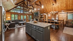 Une cuisine spacieuse dotée d’un grand îlot central, de poutres en bois et d’une cheminée en pierre.