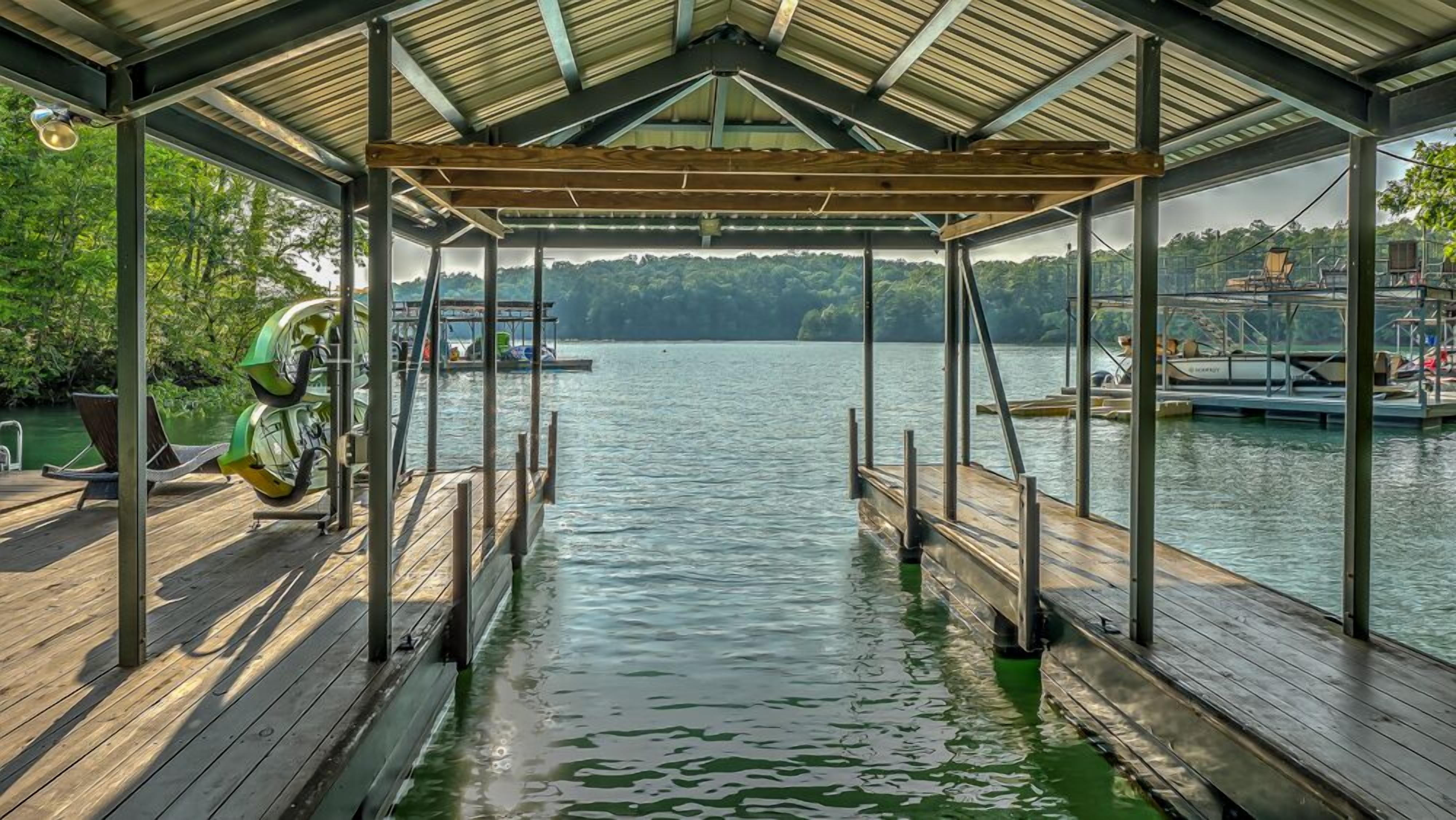 A covered dock extending into a lake with a view of the surrounding forest and docked boats.
