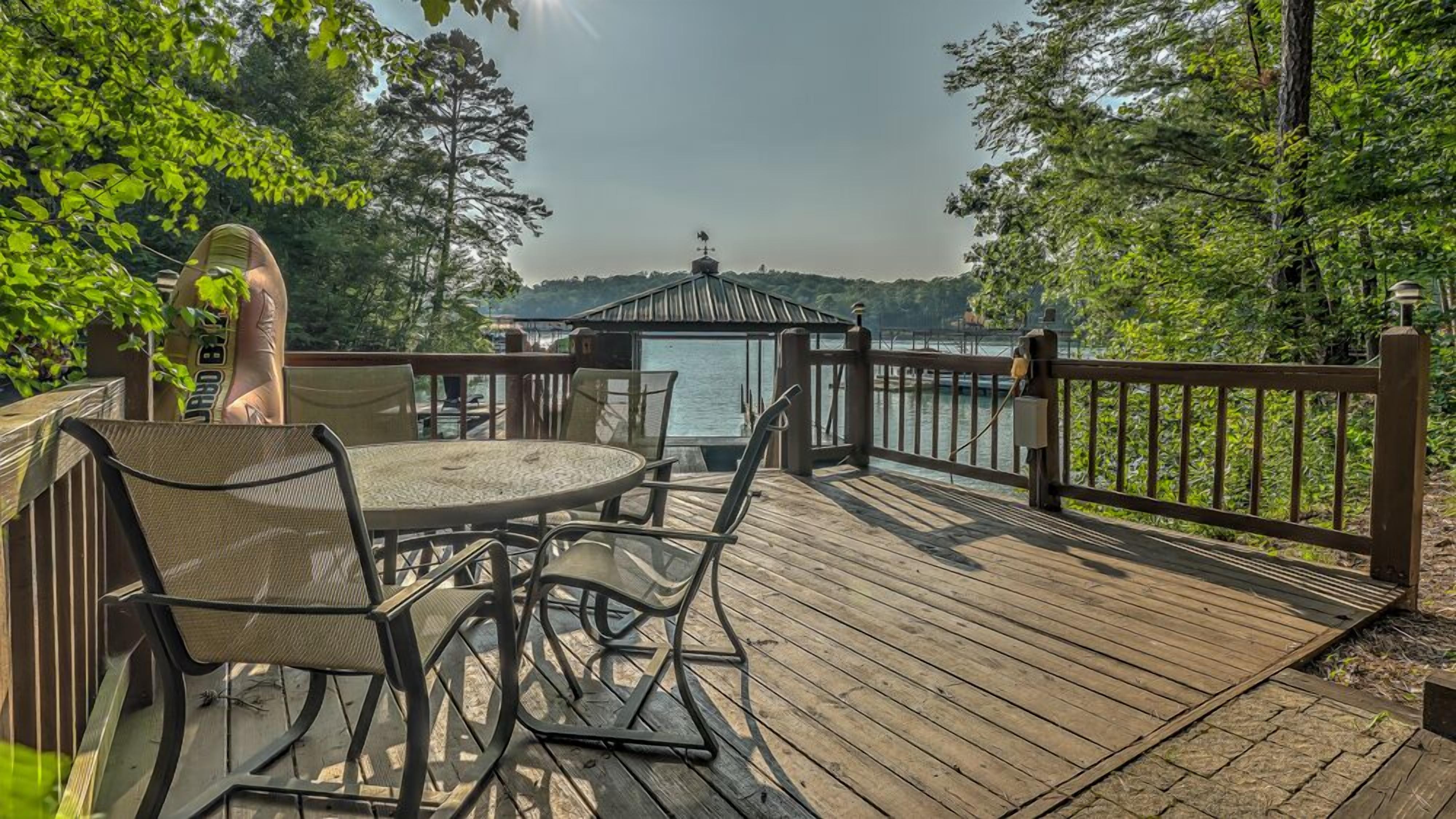 A wooden deck with a table and chairs, overlooking a body of water and a gazebo.