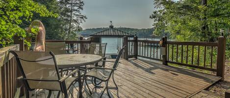 A wooden deck with a table and chairs, overlooking a body of water and a gazebo.