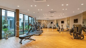 A spacious gym with cardio machines, weight stations, and large windows offering a view of the outdoors. - Spa Du Cap 2 bedroom apartment (Antibes)