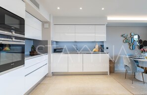 Eine moderne Küche mit weißen Schränken, einem eingebauten Backofen und einem Essbereich mit Tisch und Stühlen.