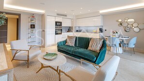 A modern living room with a green sofa, white armchairs, and a round coffee table. - Spa Du Cap 2 bedroom apartment (Antibes)