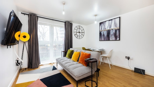 Un salon moderne avec un canapé, un téléviseur à écran plat, une horloge et un tableau accroché au mur.