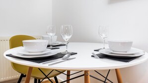 Une table de salle à manger ronde, avec de l’assiette blanche, des bols, des couverts et des verres à vin, le tout disposé pour deux personnes.