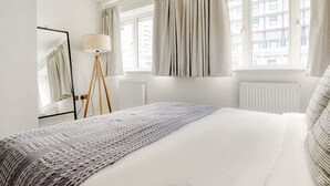 Una camera d'albergo con un grande letto, una lampada da terra e tende alle finestre.