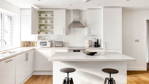 Una cucina moderna con mobili bianchi, un'isola centrale con sgabelli, un forno a microonde, un tostapane, un bollitore e una macchina da caffè.