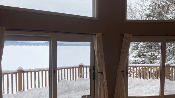 Una habitación con amplios ventanales que dan a una terraza nevada y una masa de agua.