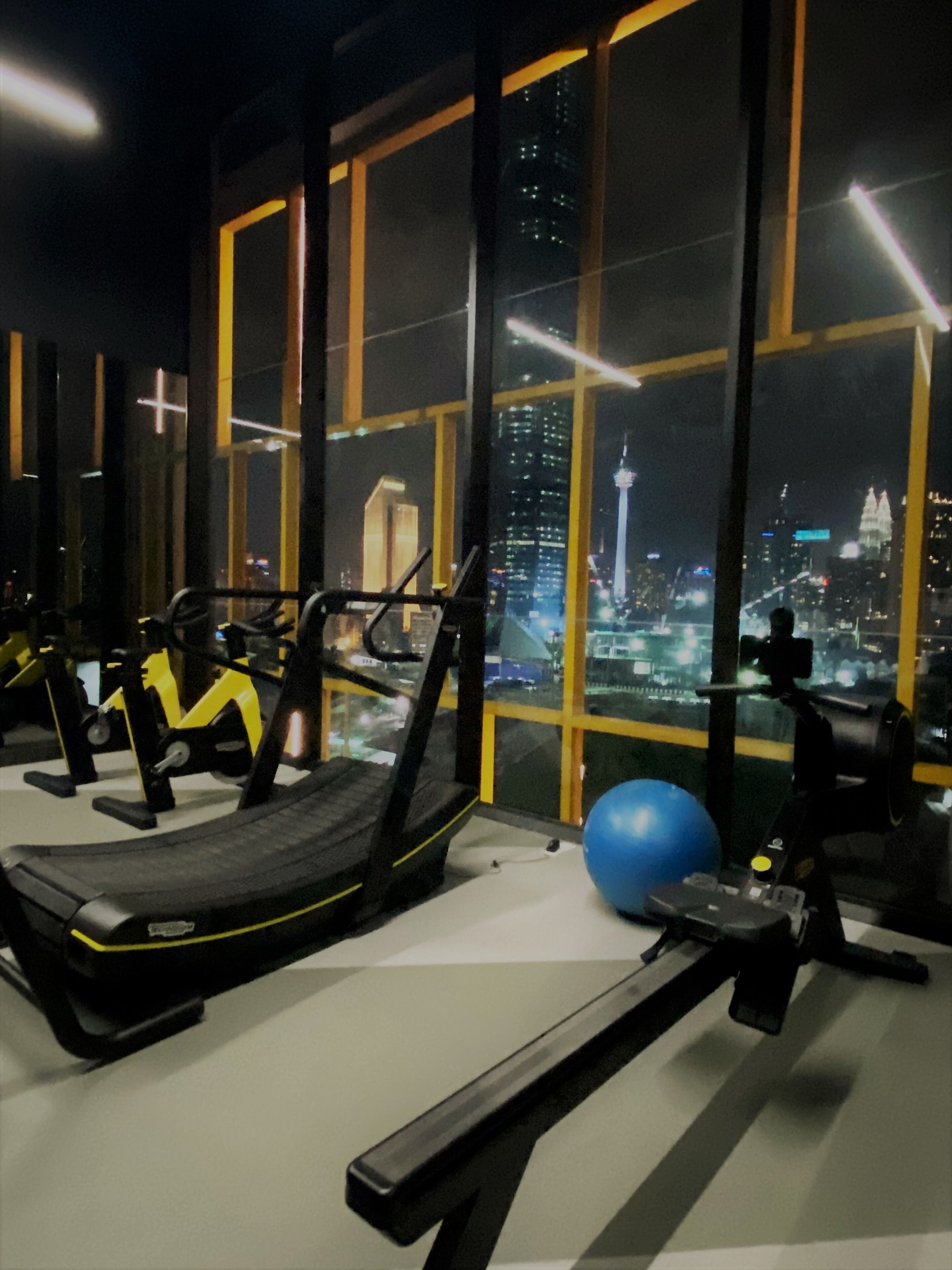 A gym with exercise equipment and a large window overlooking a cityscape at night.